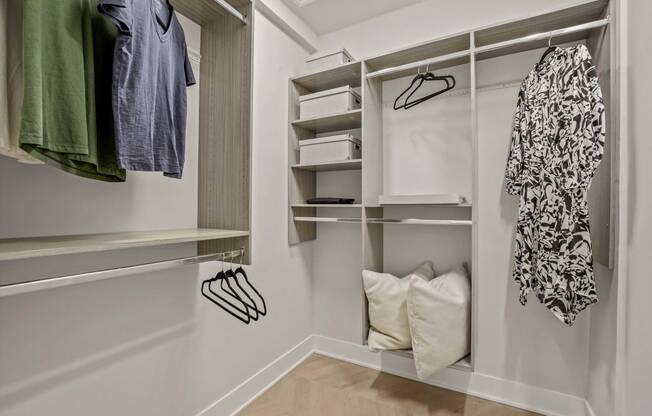 a walk in closet with white walls and shelves and a hanging rack with clothes