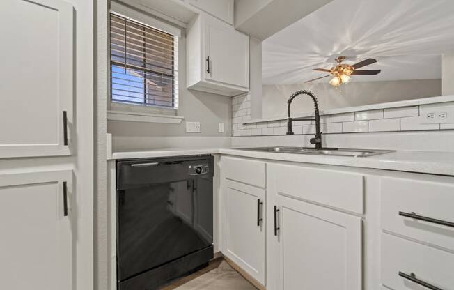 an empty kitchen with white cabinets and a black dishwasher