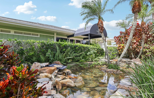 A garden with a pond and a house in the background.