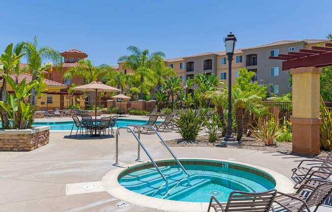 A pool surrounded by chairs and plants with a building in the background.