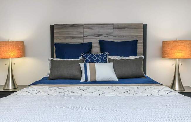 A bed with a white comforter and blue pillows is flanked by two lamps.