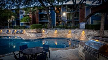 A pool area with a table and chairs is lit up at night.