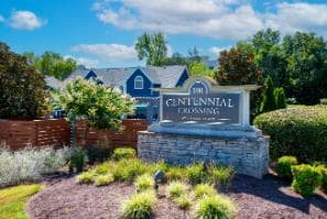 A sign that says Centennial Crossing in front of a blue house.