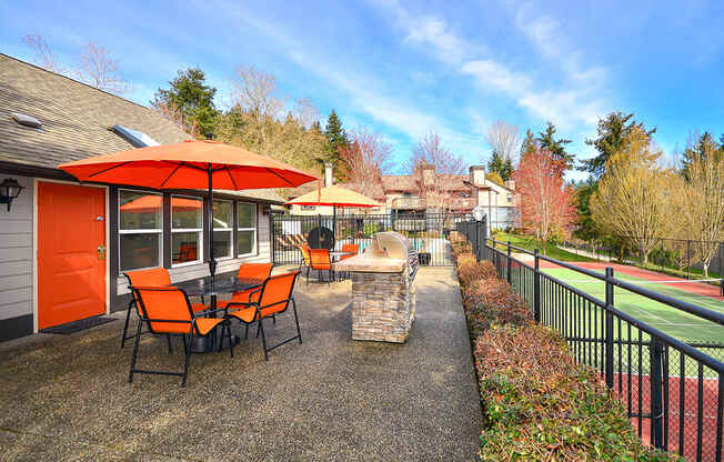A patio with orange chairs and a table is surrounded by a black fence.
