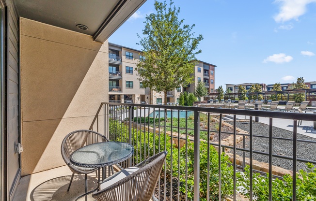 A balcony with a chair and table overlooking a pool and buildings.