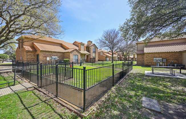 A black fence surrounds a green lawn in front of a brick building.