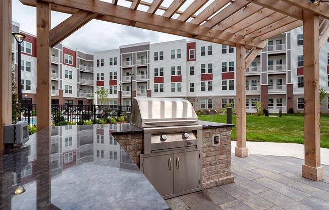A BBQ grill is situated under a wooden pergola in a courtyard.