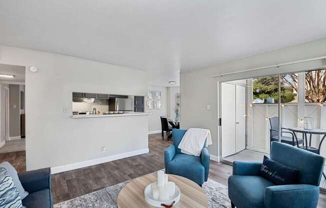 a living room with blue couches and chairs and a kitchen with a sliding door