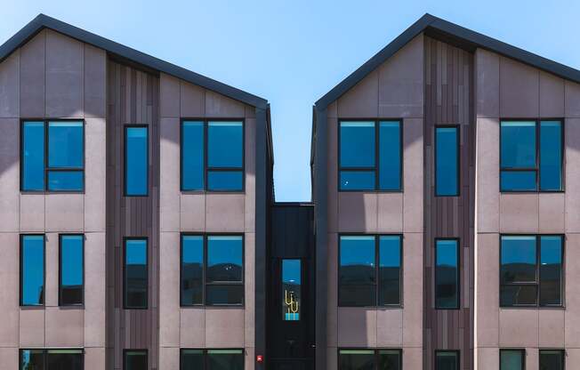 Two identical buildings with brown and beige facades and blue sky in the background.