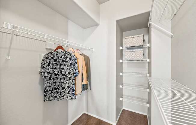 A white closet with clothes hanging and shelves.