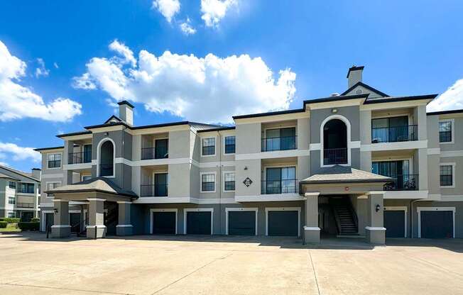 An apartment building with an arched entrance and vibrant greenery at Saxony at Chase Oaks Apartments in Dallas, TX, showcasing the property's elegant architecture.