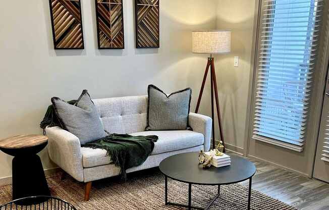 A living room with a grey couch, a black metal chair, and a table with a lamp on it.