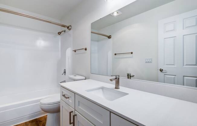 Everett, Washington, Apartments - Woodbrook - Bathroom with Wood-Style Flooring, Shower and Tub Combo, Oversized Mirror, Sink Vanity with Modern Hardware, and White Cabinetry.