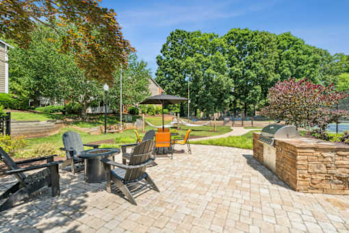A patio with chairs and a table is surrounded by trees.