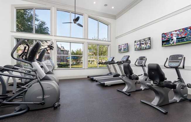 A gym with a row of stationary bikes and a fan.