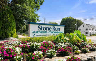 A sign for Stone Run Apartments is surrounded by flowers.