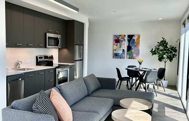 a living room with a couch table and chairs and a kitchen in the background at DOCK 59 APARTMENTS, PORTLAND, OR