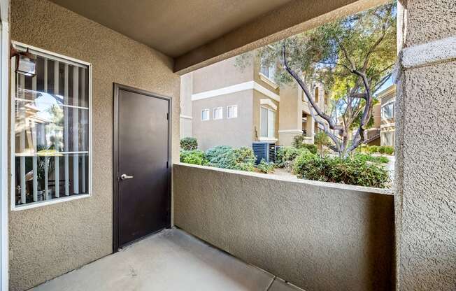 A balcony with a door and a window overlooking a building and trees.