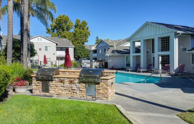 The Legacy Apartments pool area with two built-in gas barbecue grills facing the pool and backside of the clubhouse