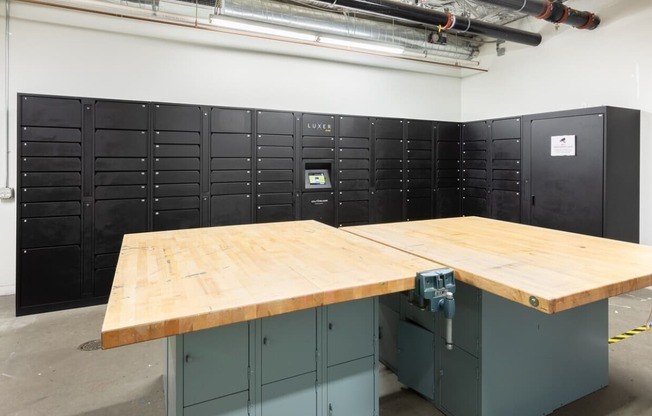 a large wooden table sits in the middle of a room full of black lockers