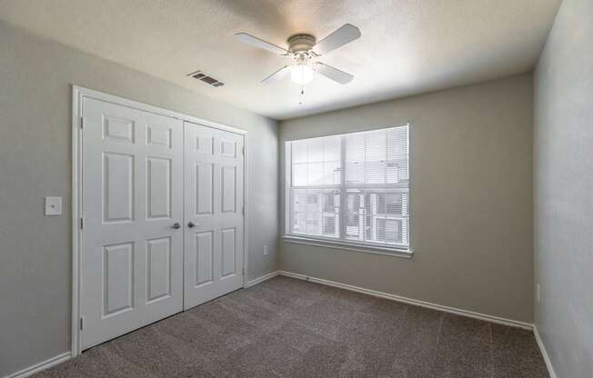 an empty bedroom with a ceiling fan and a window