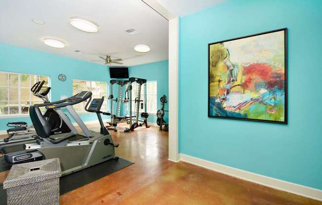 A gym with a treadmill, elliptical machines, and a painting on the wall.