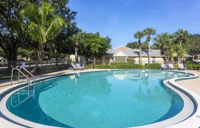 a swimming pool with palm trees and a house in the background at Aqua Bay Apartments in Naples, FL 34116
