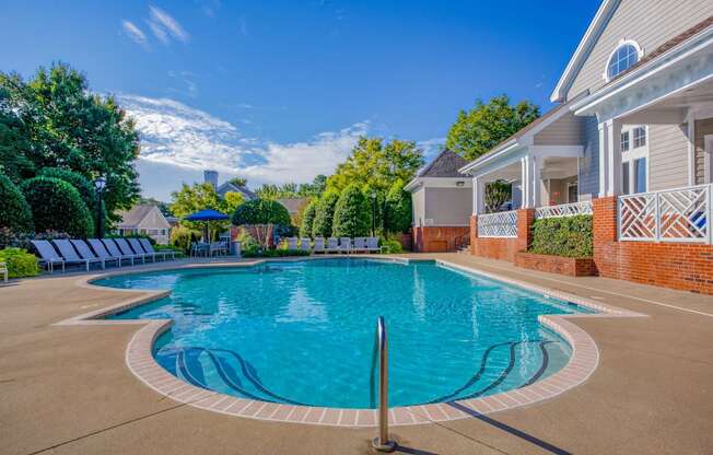 A large outdoor swimming pool surrounded by a brick wall and lounge chairs.