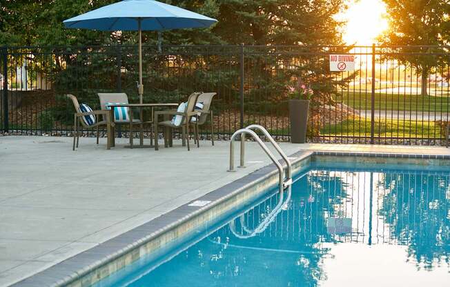 a swimming pool with an umbrella and a table with chairs at The Winhall of Williams Pointe Apartments, Waukee, IOWA
