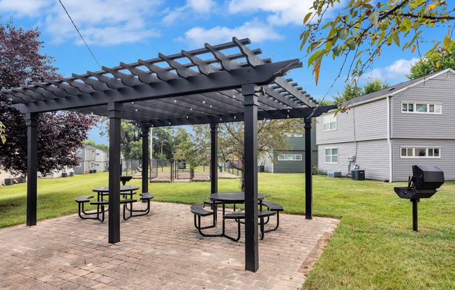 a pergola with picnic tables on a brick patio