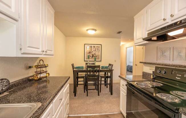 A kitchen with a black stove top oven and a dining table with chairs at Bishop's Court Apartments, California, 95670