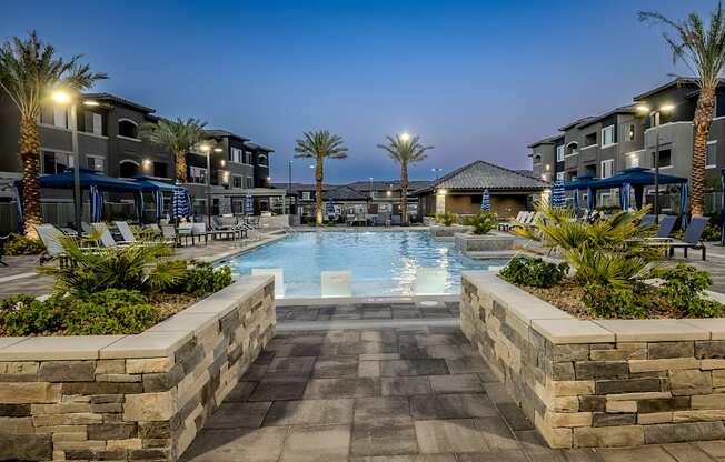 A swimming pool surrounded by stone walls and palm trees at dusk.