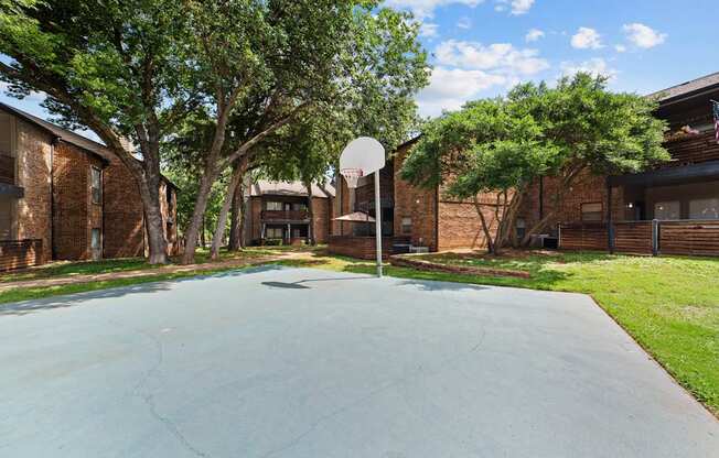 A basketball court is surrounded by trees and brick buildings.