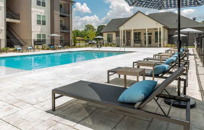 a swimming pool with chaise lounge chairs and umbrellas in front of a building