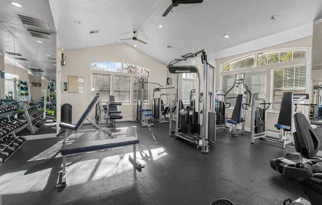 A spacious gym with a variety of equipment and a fan on the ceiling.