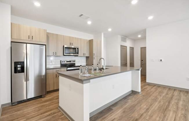 a kitchen with a large island and a stainless steel refrigerator at The Depot in The Depot Raymore, MO 64083