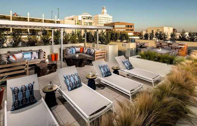 A rooftop patio with lounge chairs and cushions overlooking a cityscape.
