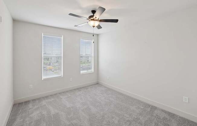 A room with a ceiling fan and two windows.
