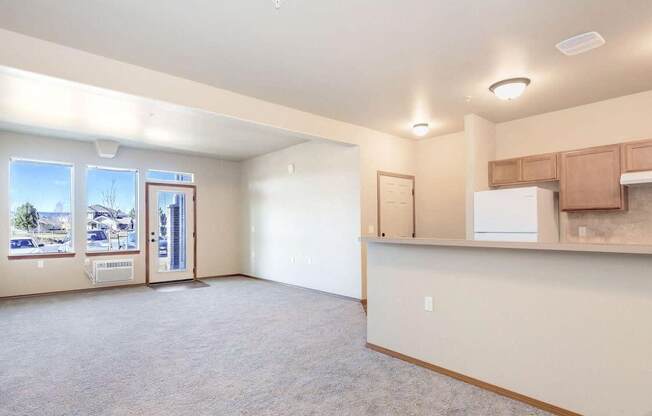 an empty living room with a kitchenette and a door leading to a balcony