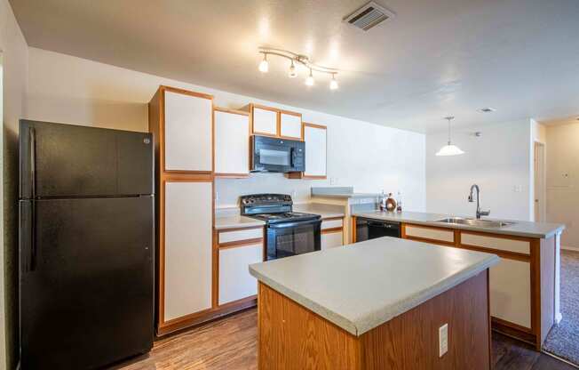 Kitchen with a white top island, black fridge, stainless steel sink, black microwave and blank oven/stovetop