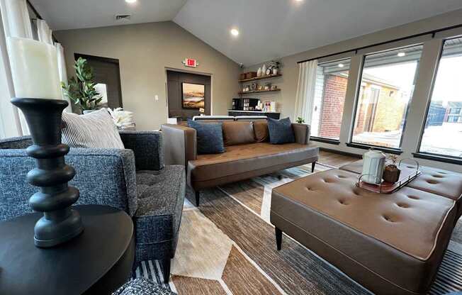 A living room with a grey couch, a brown ottoman, and a black table with a candle on it.