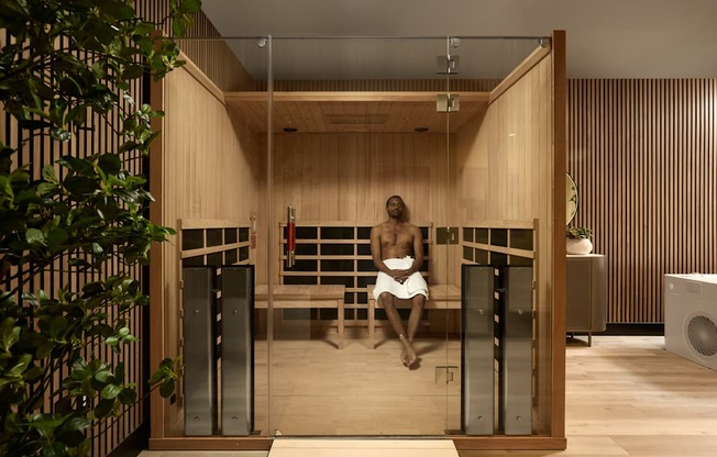 A man is sitting in a sauna with wooden walls and a bench.