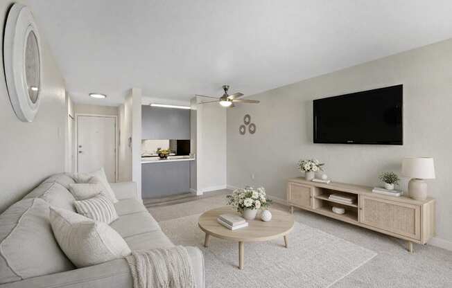 A living room with a grey couch, a wooden coffee table, and a flat screen TV mounted on the wall.