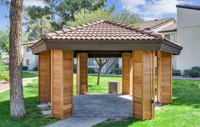 A wooden gazebo with a tiled roof is situated in a grassy area.
