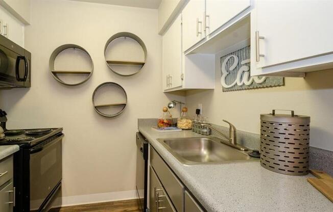 Dog Friendly Apartments in Mesa AZ - Mesa Station - Kitchen with Grey Speckled Countertops, White Upper Cabinetry, Grey Lower Cabinetry, Black Appliances, and Wood-Style Flooring