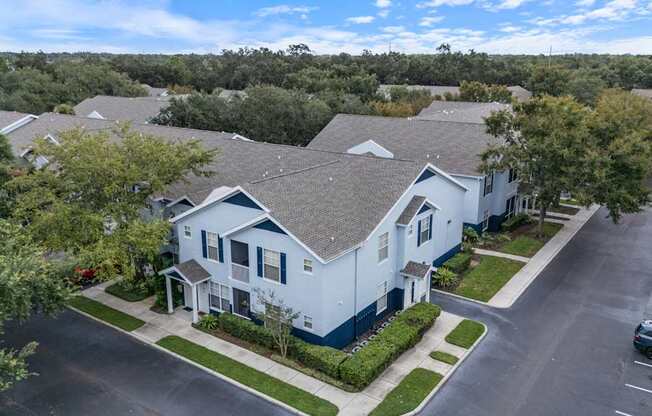 A white house with a grey roof is surrounded by greenery and other similar houses.