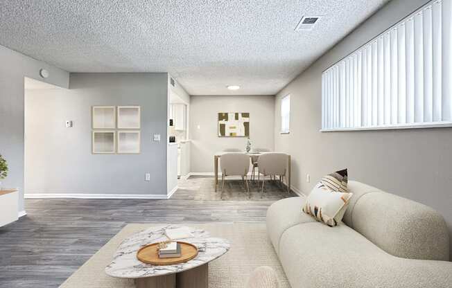 A living room with a couch, coffee table, and a dining area in the background.