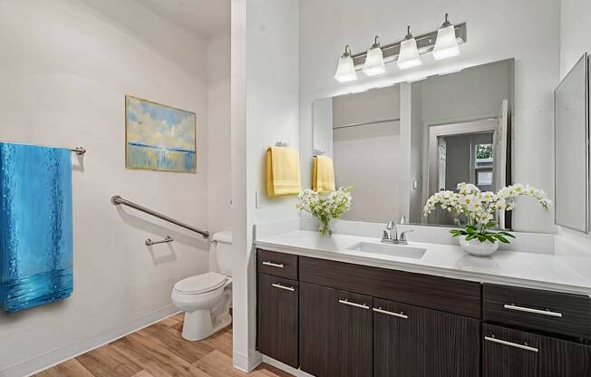 A bathroom with a blue towel and a painting of a sunny sky.