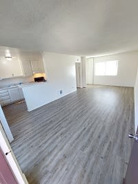 an empty living room with a kitchen in the background