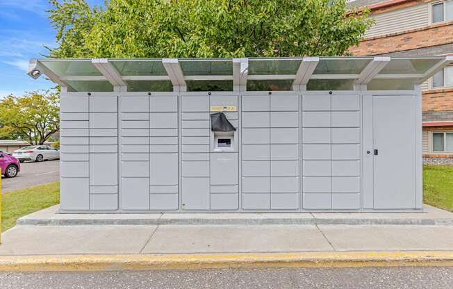 A grey utility box with a black door and a small window is on a sidewalk.